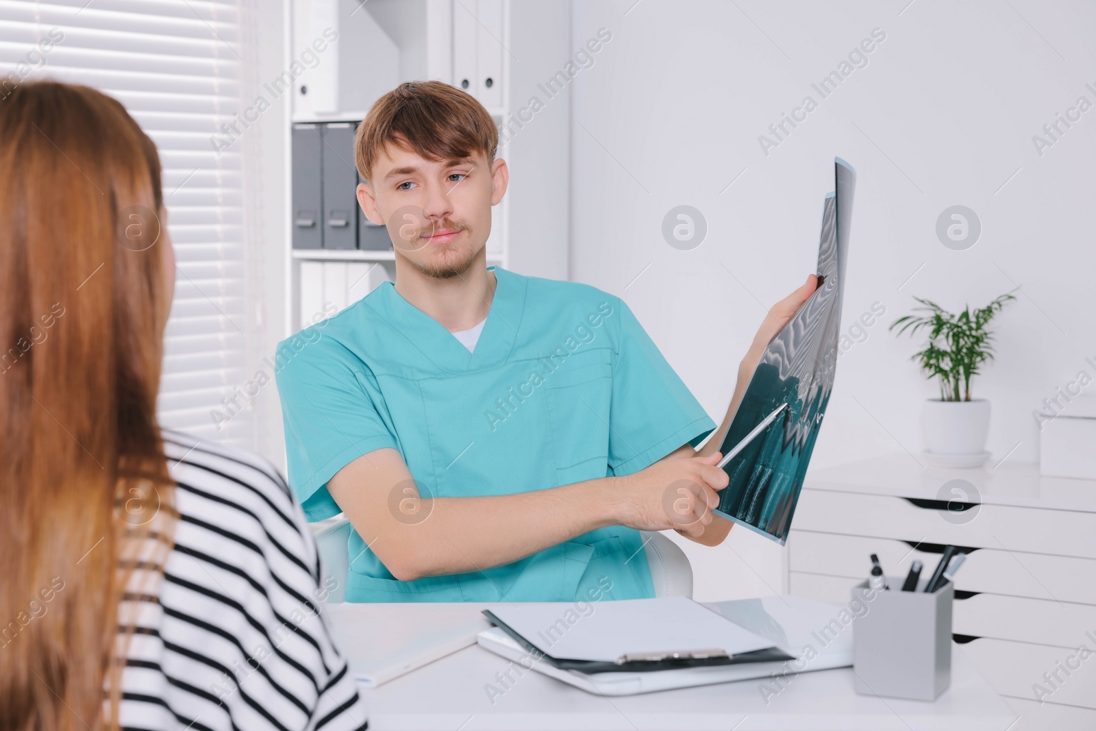 Photo of Doctor with neck MRI image consulting patient in clinic