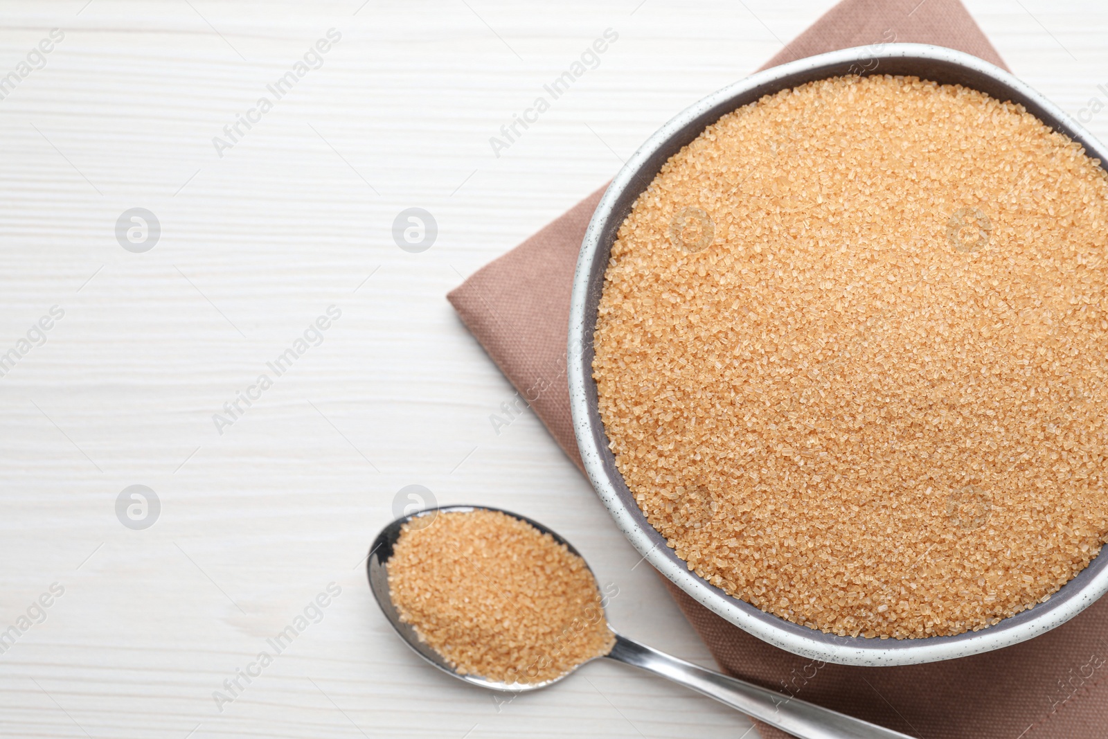 Photo of Brown sugar in bowl and spoon on white wooden table, flat lay. Space for text