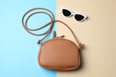 Photo of Stylish woman's bag with sunglasses on color background, flat lay