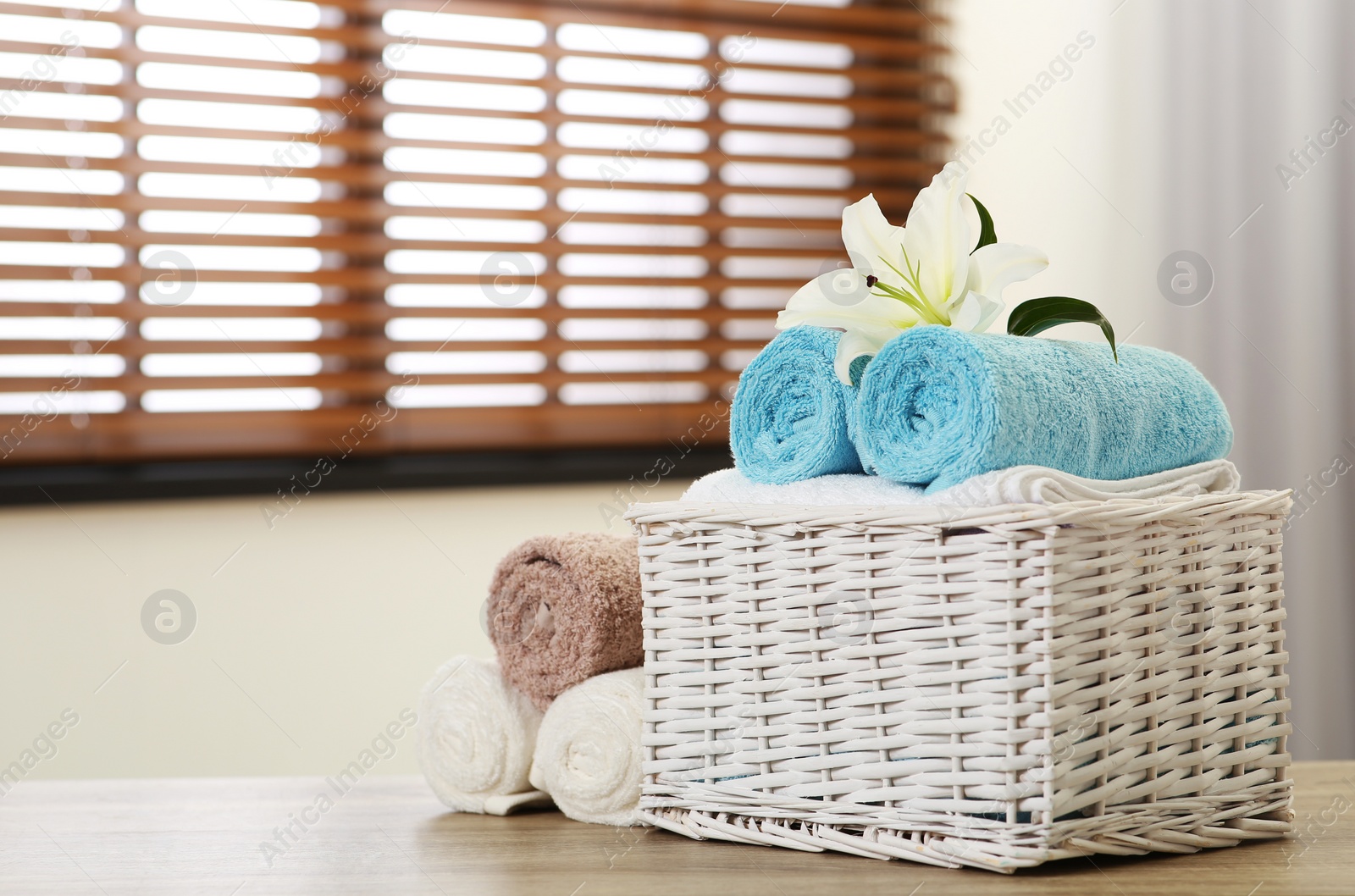 Photo of Wicker basket with clean towels and lily  on table indoors. Space for text