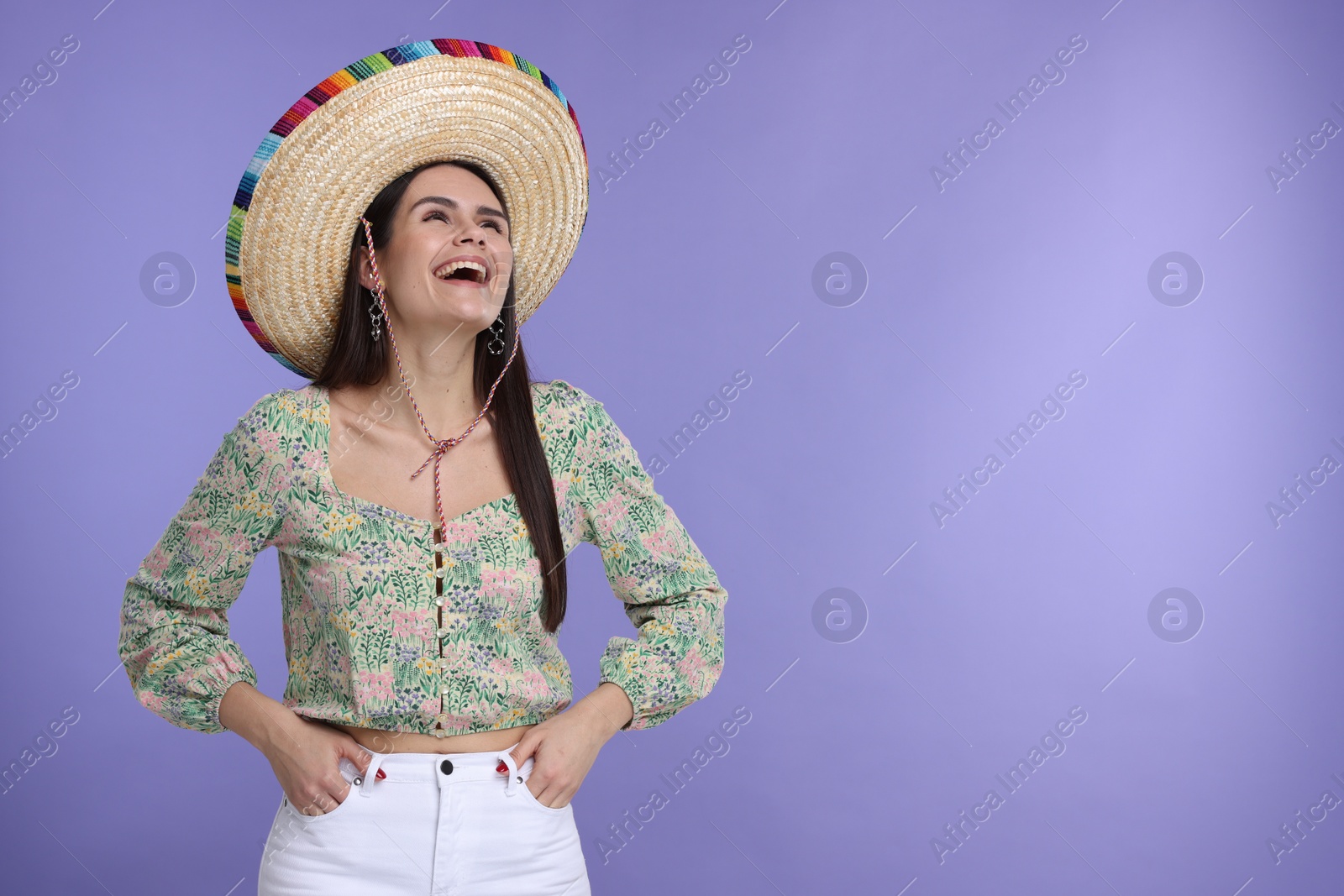 Photo of Young woman in Mexican sombrero hat on violet background. Space for text