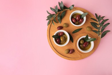 Photo of Wooden tray with different ripe olives and leaves on pink background, flat lay. Space for text