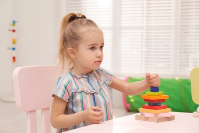 Photo of Cute child playing with colorful wooden stacker at table in room