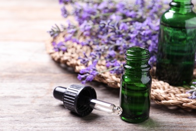 Photo of Bottles of essential oil and lavender flowers on wooden table