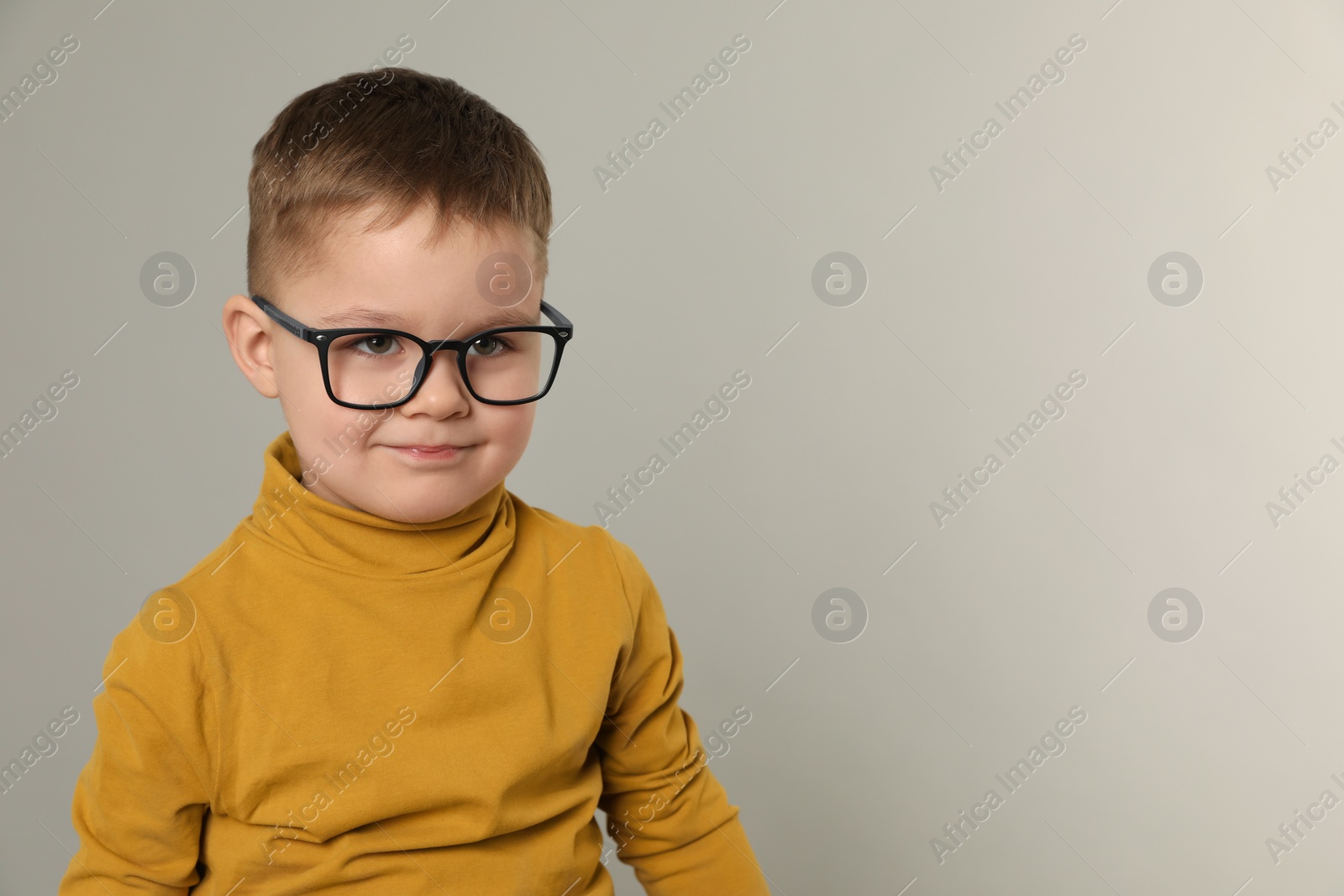 Photo of Cute little boy in glasses on light grey background. Space for text