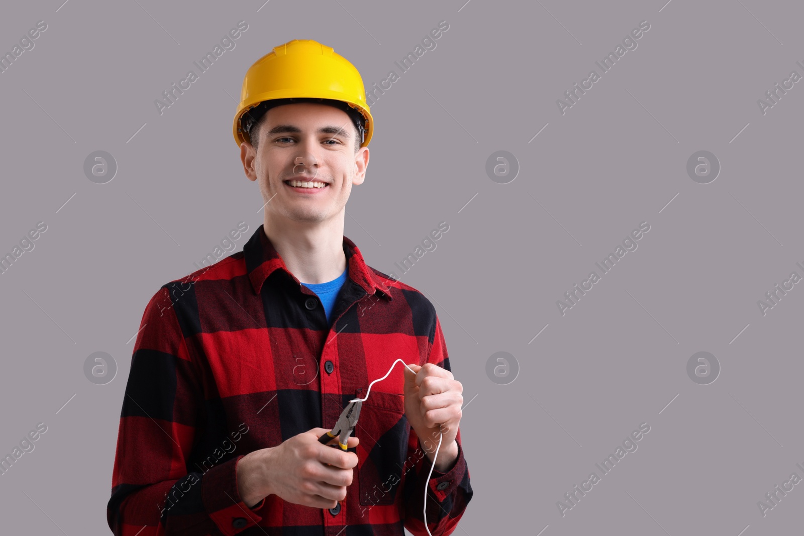 Photo of Young man holding pliers and wire on grey background, space for text