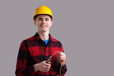 Photo of Young man holding pliers and wire on grey background, space for text