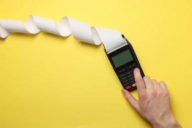 Photo of Man using payment terminal with thermal paper for receipt on yellow background, top view