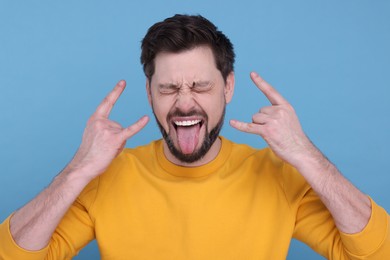 Photo of Happy man showing his tongue and making rock gesture on light blue background