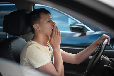 Photo of Tired man yawning in his modern car