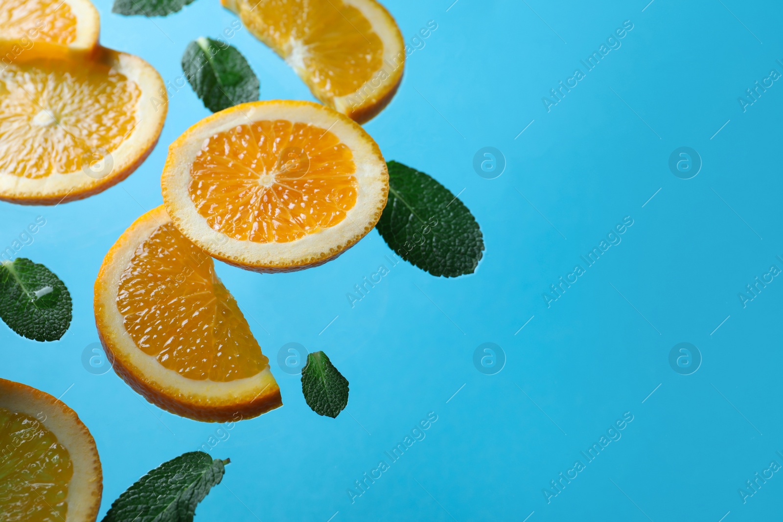 Photo of Tasty ripe oranges and green leaves falling on light blue background. Space for text