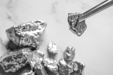 Photo of Tweezers with silver nugget above pile on white marble table, closeup