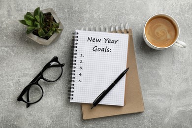 Image of Notebook with inscription New Year Goals, cup of aromatic coffee, glasses and plant on grey table, flat lay