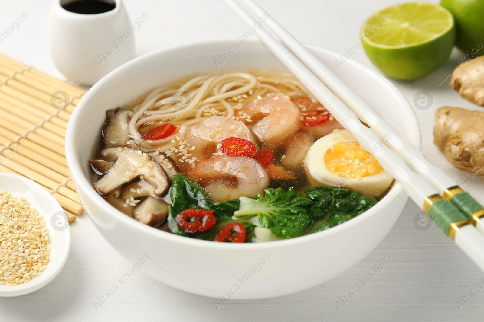 Photo of Tasty ramen with shrimps in bowl and chopsticks on white table, closeup