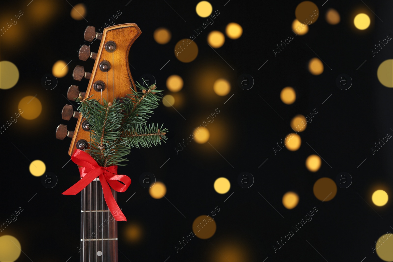 Photo of Guitar with bow and fir tree twig against blurred lights, space for text. Christmas music