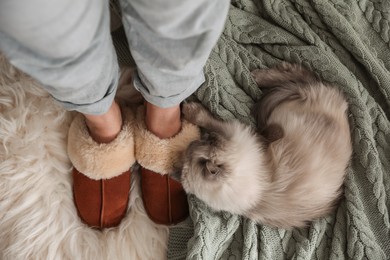 Photo of Woman in stylish soft slippers resting with cute cat at home, top view