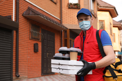 Photo of Courier in protective mask and gloves with orders near house outdoors. Food delivery service during coronavirus quarantine