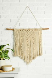 Photo of Beautiful macrame hanging on white brick wall in room. Decorative element