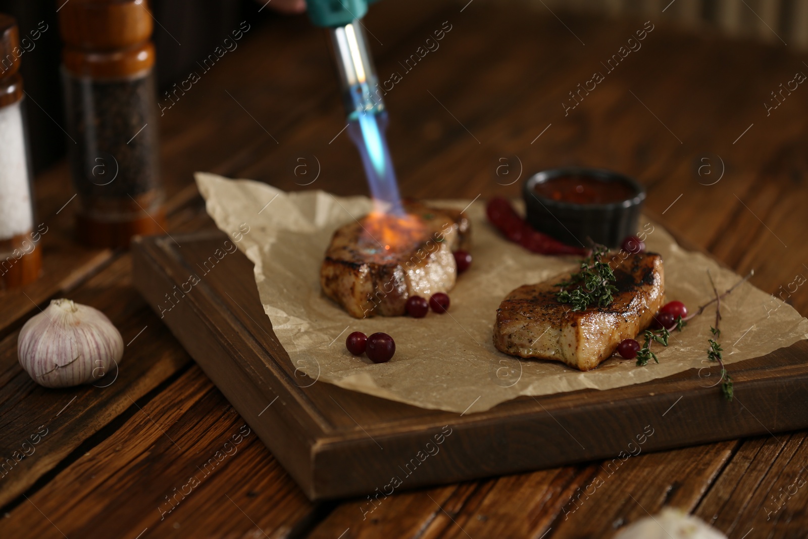 Photo of Cooking meat medallions with manual gas burner on wooden table in photo studio. Food stylist