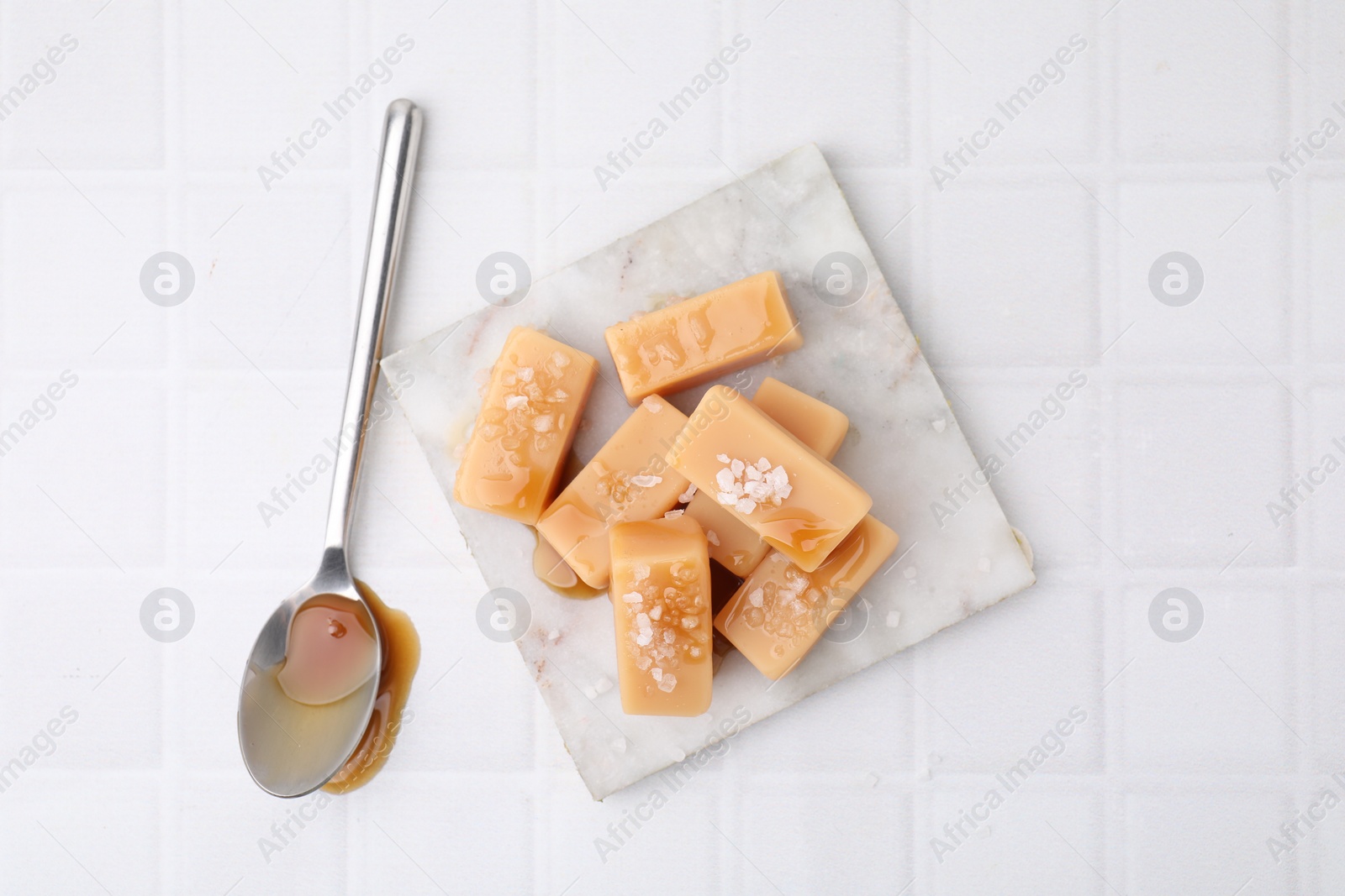 Photo of Delicious candies with sea salt and caramel sauce on white tiled table, top view