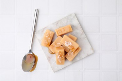 Photo of Delicious candies with sea salt and caramel sauce on white tiled table, top view