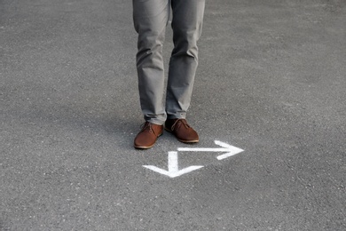 Photo of Man standing near arrows on asphalt. Choice concept