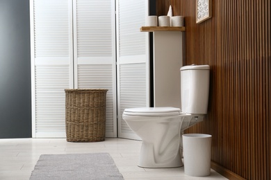 Photo of White toilet bowl near wooden wall in modern bathroom interior