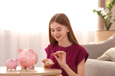 Photo of Teen girl with piggy banks and money at home