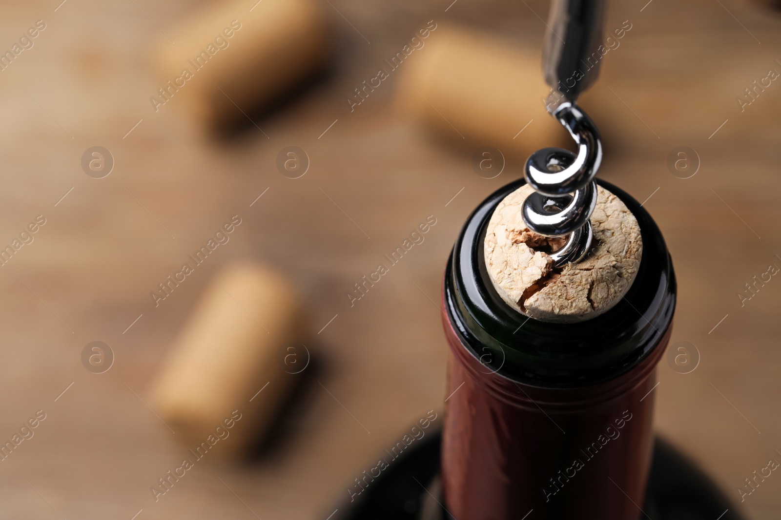 Photo of Opening wine bottle with corkscrew on table, closeup. Space for text