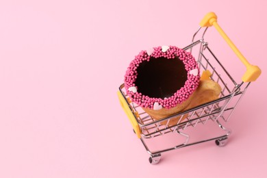 Photo of Delicious edible biscuit coffee cup decorated with sprinkles in shopping cart on pink background, space for text