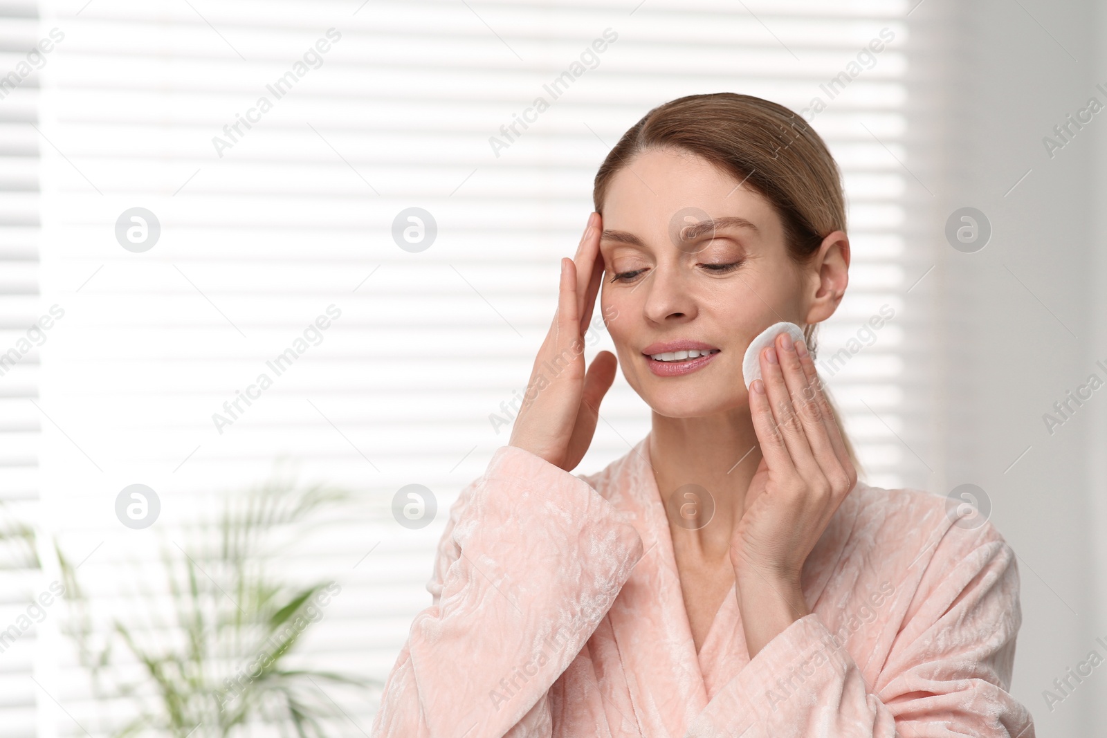 Photo of Beautiful woman removing makeup with cotton pad indoors