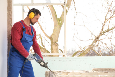 Worker using rotary drill hammer for window installation indoors