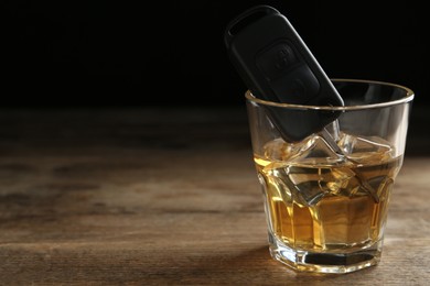 Car key in glass of alcohol on wooden table, space for text. Dangerous drinking and driving