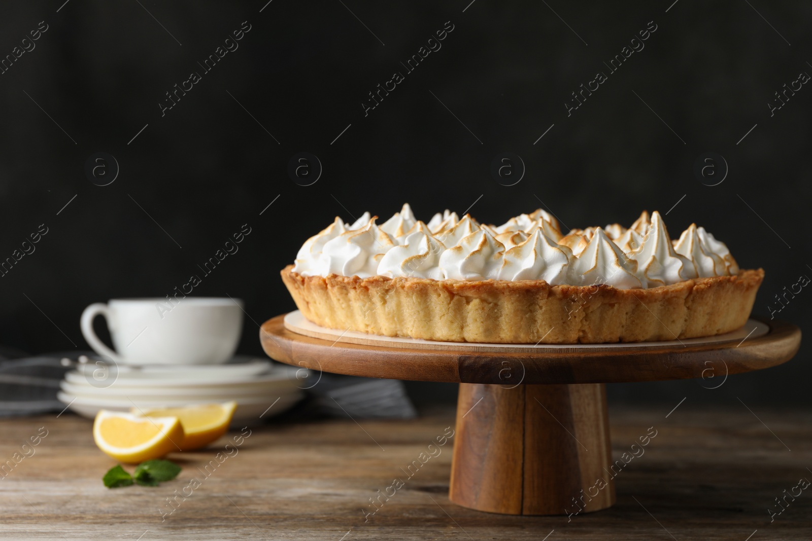 Photo of Stand with delicious lemon meringue pie on wooden table against black background