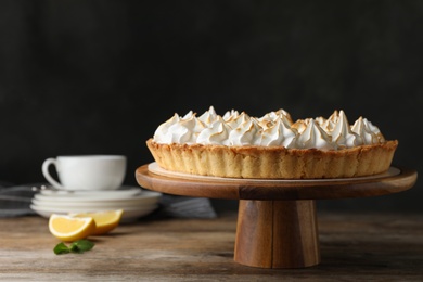 Stand with delicious lemon meringue pie on wooden table against black background