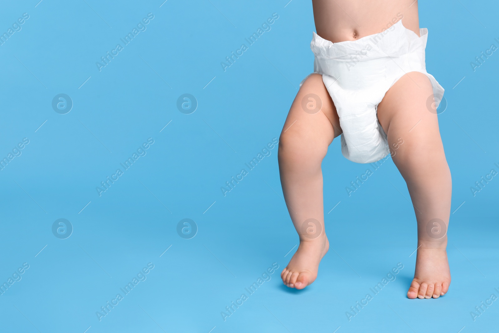 Photo of Cute baby in dry soft diaper standing on light blue background, closeup. Space for text