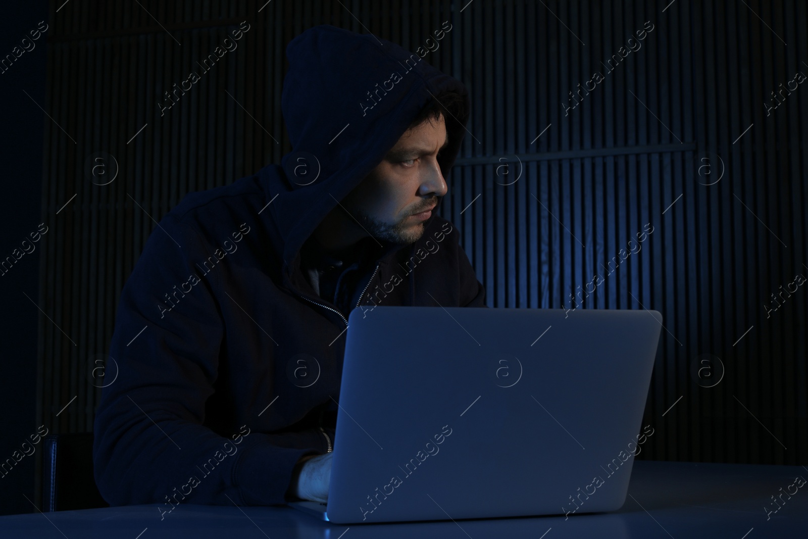 Photo of Man using laptop in dark room. Criminal offence