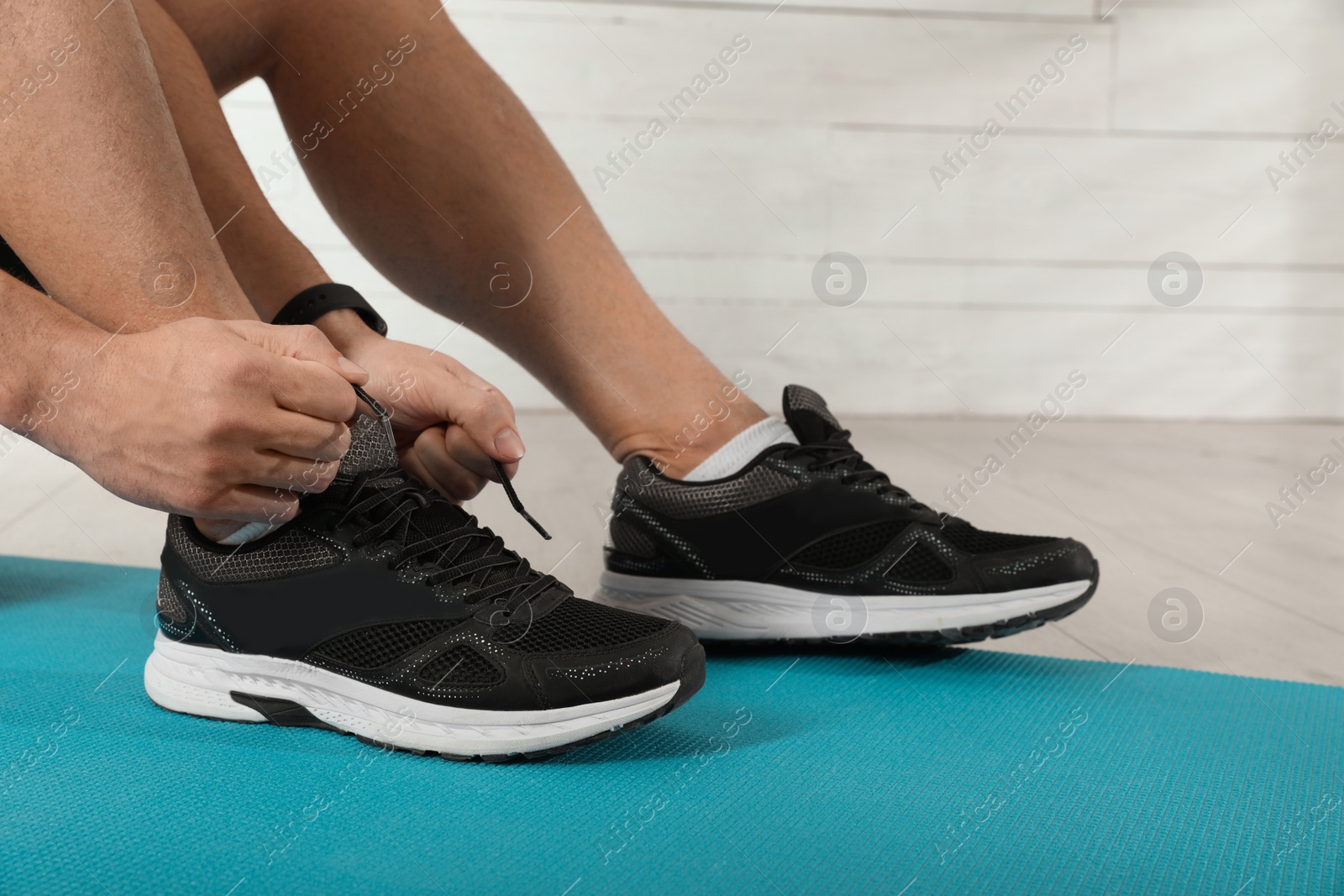 Photo of Man tying sneaker's shoelaces on exercise mat indoors, closeup