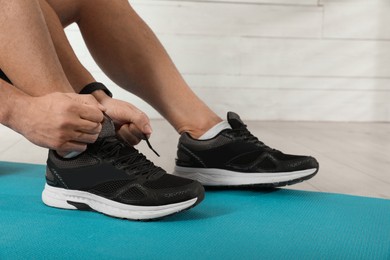 Man tying sneaker's shoelaces on exercise mat indoors, closeup