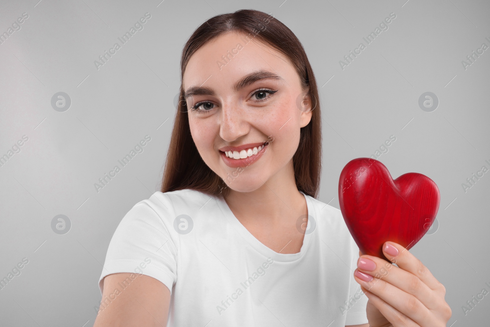 Photo of Smiling woman holding red heart on light grey background