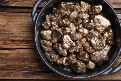 Pan of gold nuggets on wooden table, top view