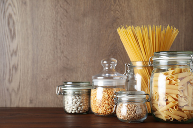 Photo of Glass jars with different types of groats and pasta on wooden table