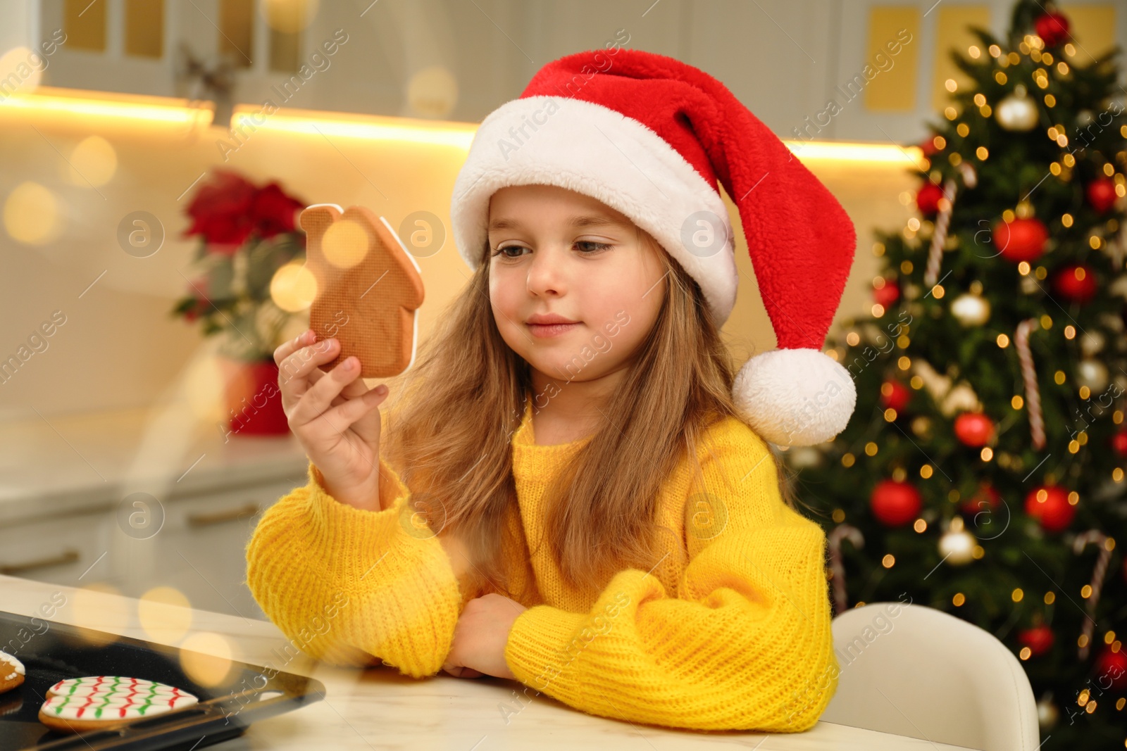 Photo of Cute little girl with freshly baked Christmas gingerbread cookie at table indoors