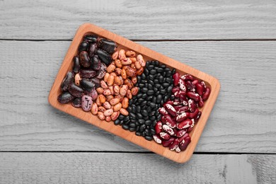 Photo of Plate with different kinds of dry kidney beans on light grey wooden table, top view