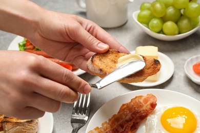 Woman spreading butter on toast at table, closeup. Buffet service