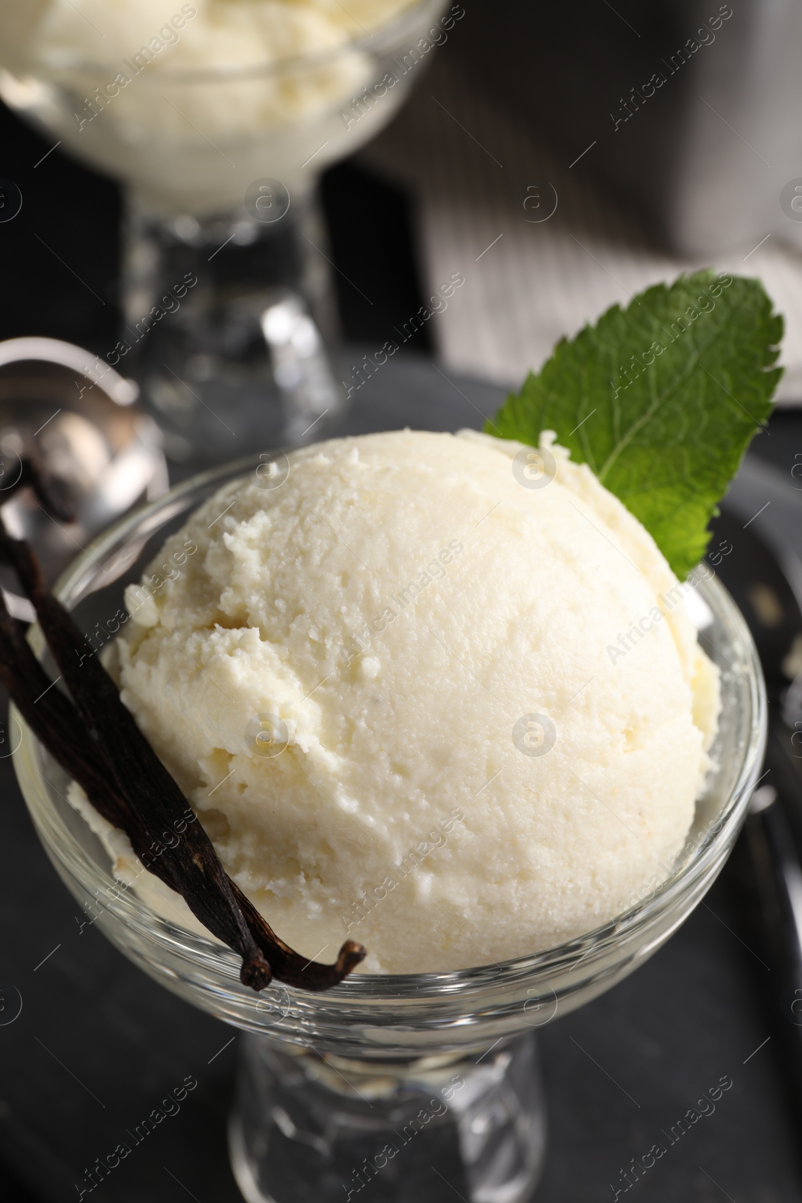 Photo of Tasty ice cream with vanilla pods in glass dessert bowl on table, closeup
