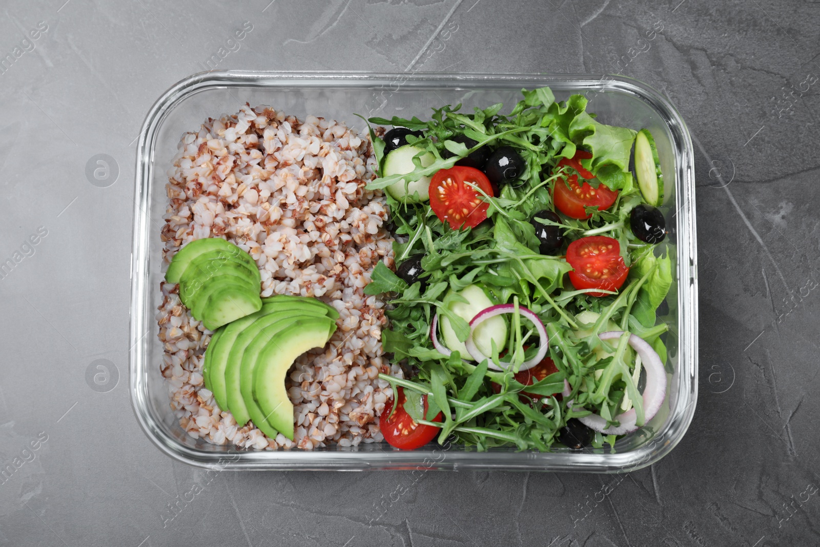 Photo of Tasty buckwheat with salad in glass container on grey table, top view