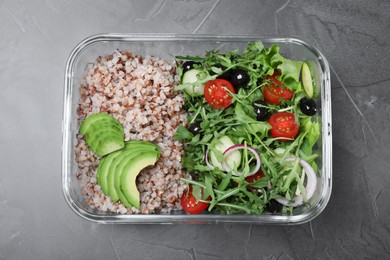 Tasty buckwheat with salad in glass container on grey table, top view