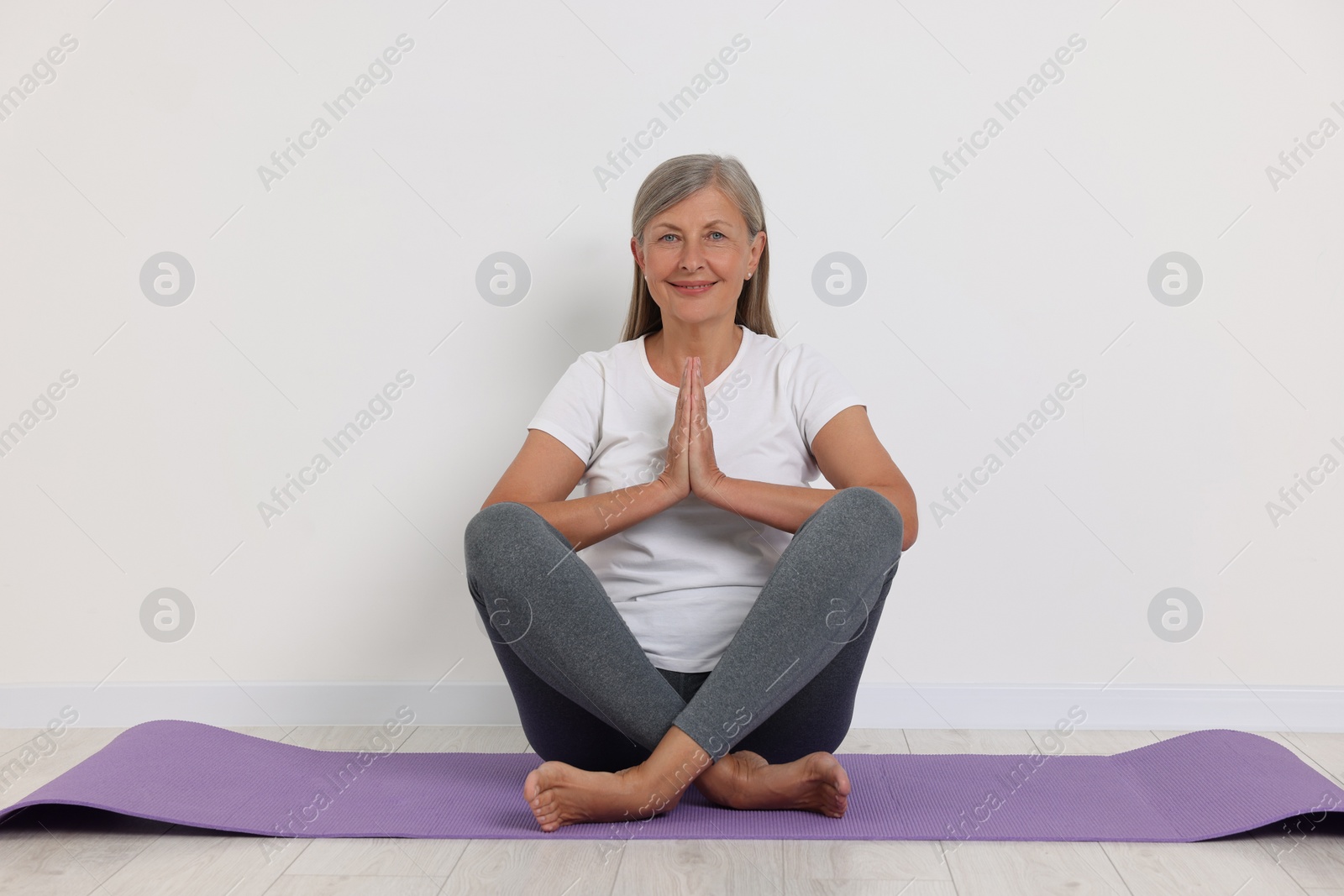 Photo of Happy senior woman practicing yoga on mat near white wall