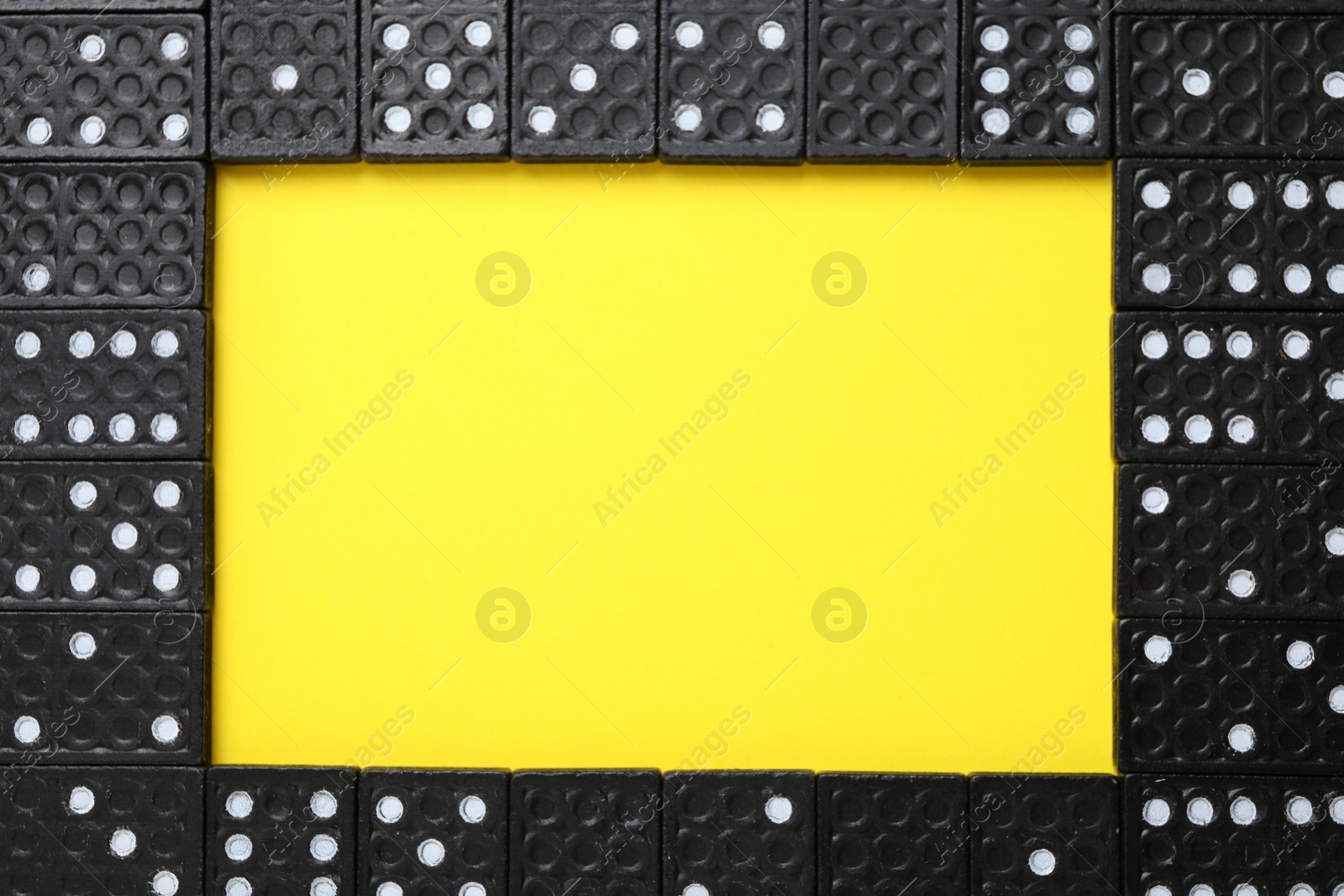 Photo of Frame of black domino tiles on yellow background, flat lay. Space for text